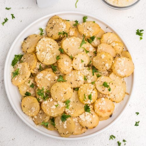 Air fryer sliced potatoes on a white plate topped with parmesan and fresh chopped parsley.