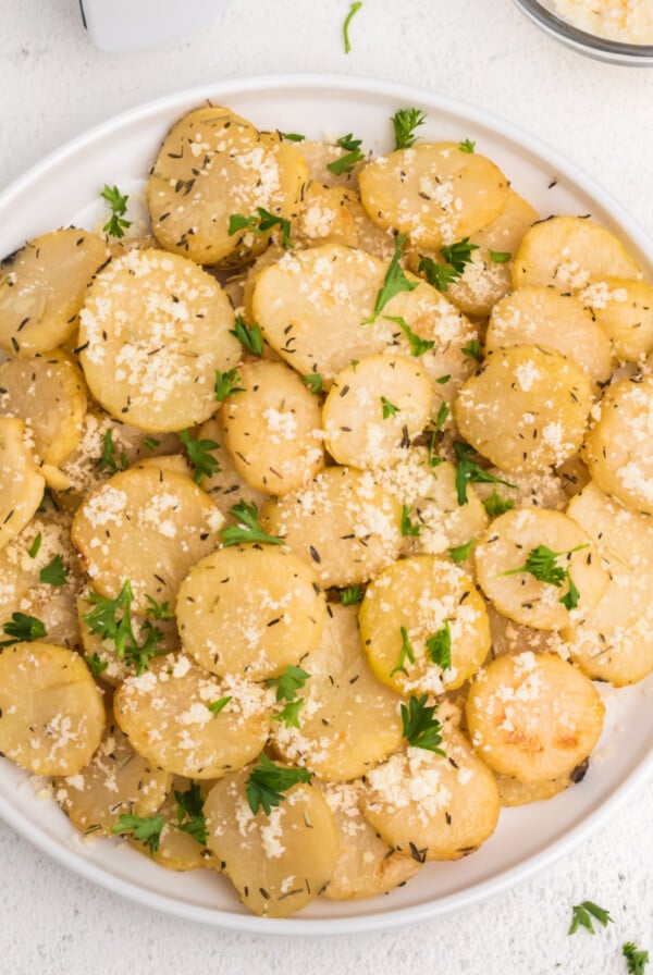 Air fryer sliced potatoes on a white plate topped with parmesan and fresh chopped parsley.