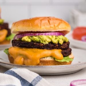 Close up photo of a black bean burger made in the air fryer and topped with mashed avocado, onion, sauce, and a bun.