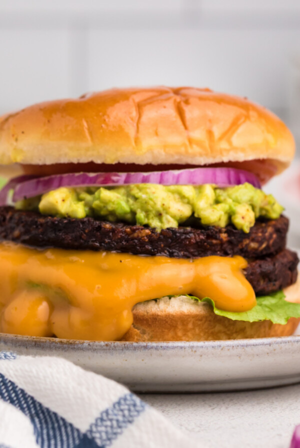 Close up photo of a black bean burger made in the air fryer and topped with mashed avocado, onion, sauce, and a bun.