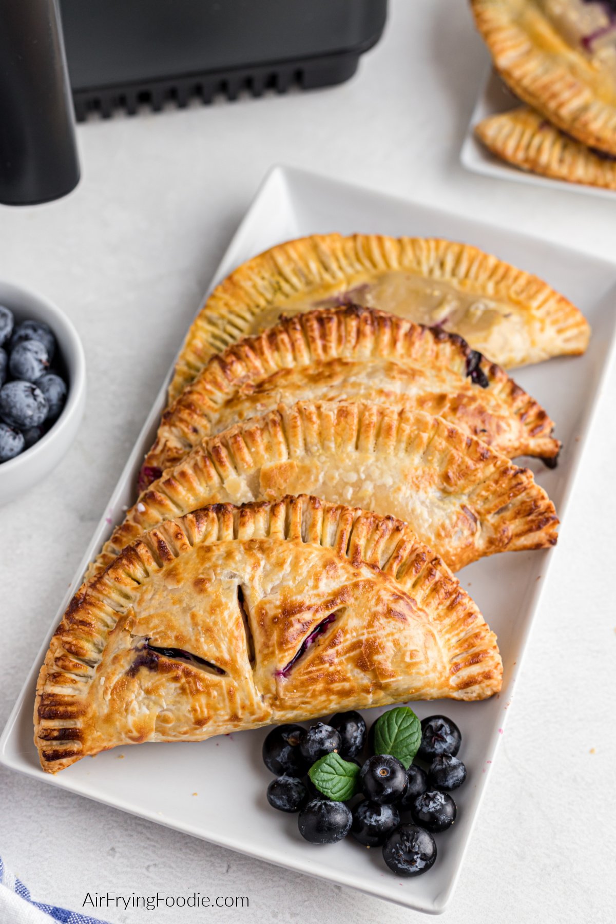 Air fryer blueberry hand pies on a plate with a side of blueberries, ready to eat.