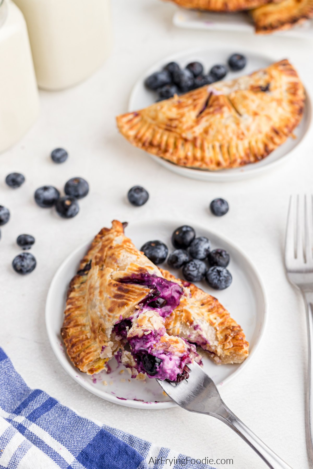 Air fryer blueberry hand pies on plates, one being eaten with a fork