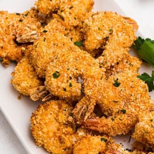 Golden breaded shrimp on a white plate garnished with parsley.
