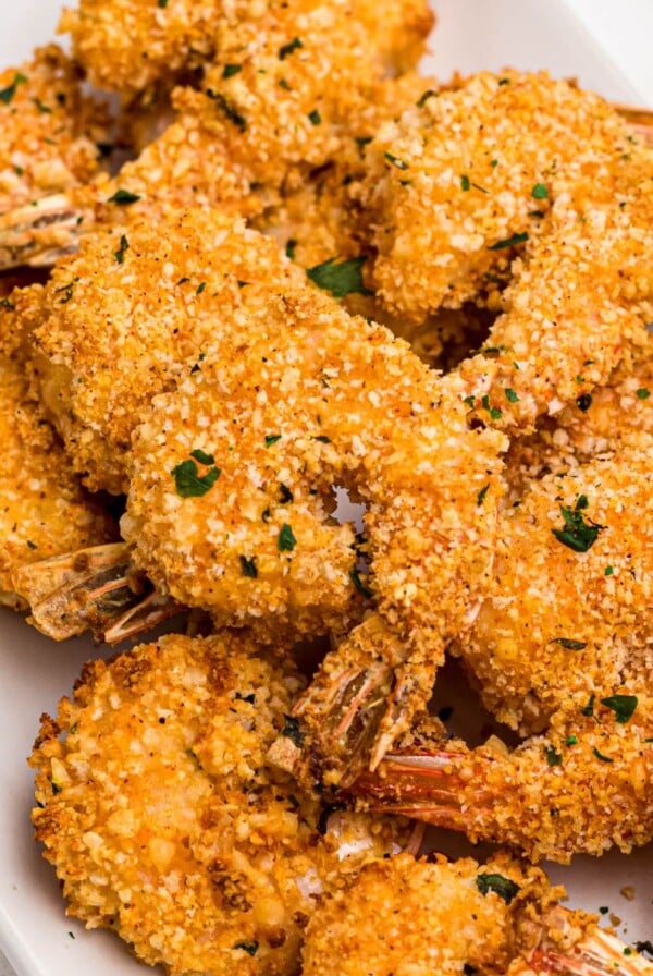 Golden breaded shrimp on a white plate garnished with parsley.