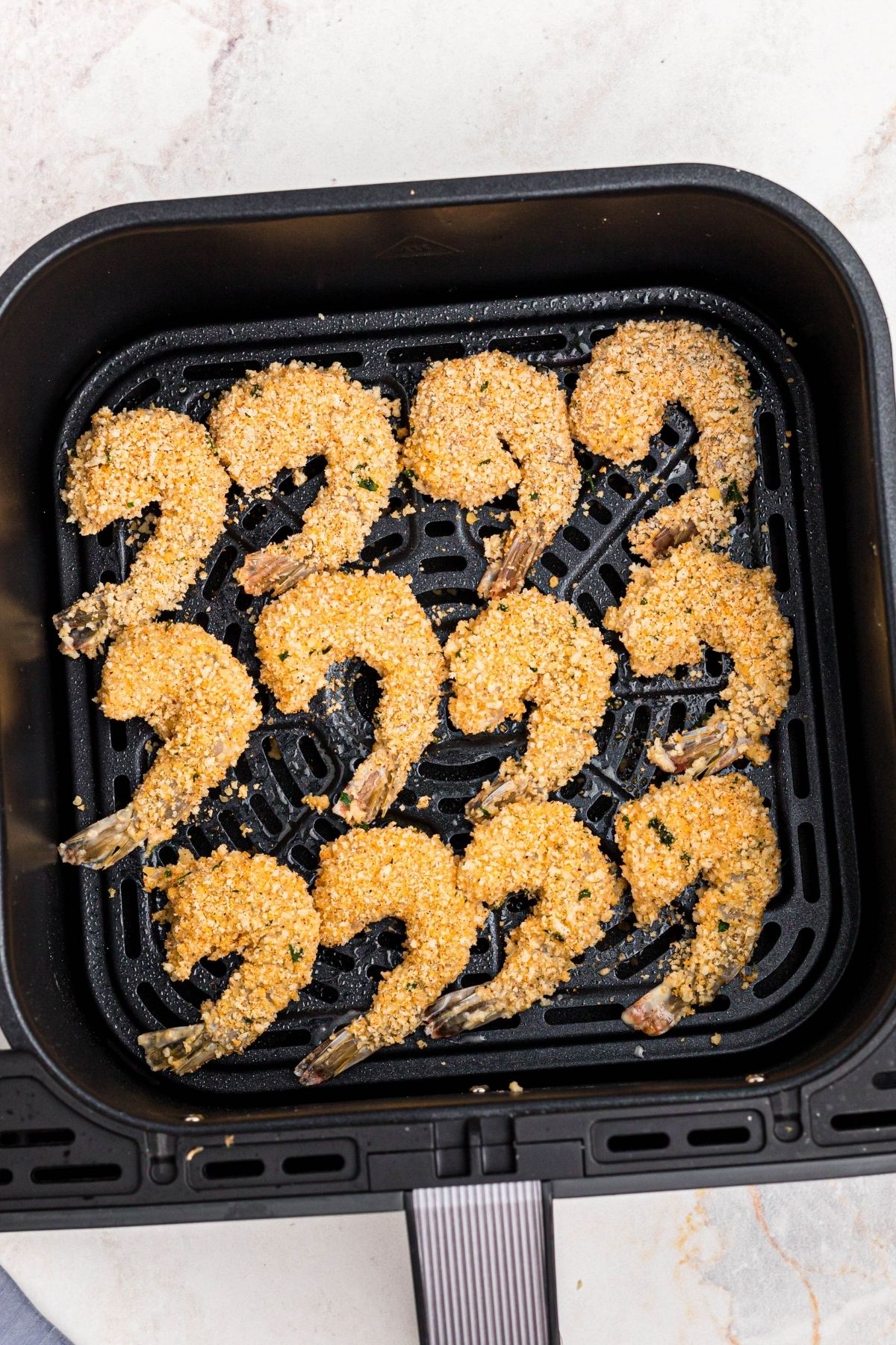 Battered and coated uncooked shrimp in the air fryer basket