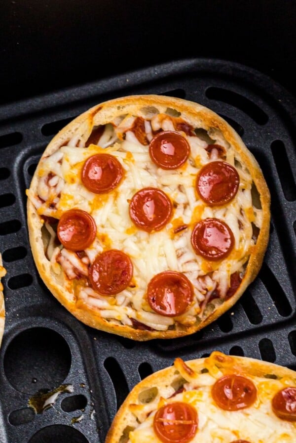 Golden crispy english muffin pizzas with melted cheese and cooked pepperonis in an air fryer basket.