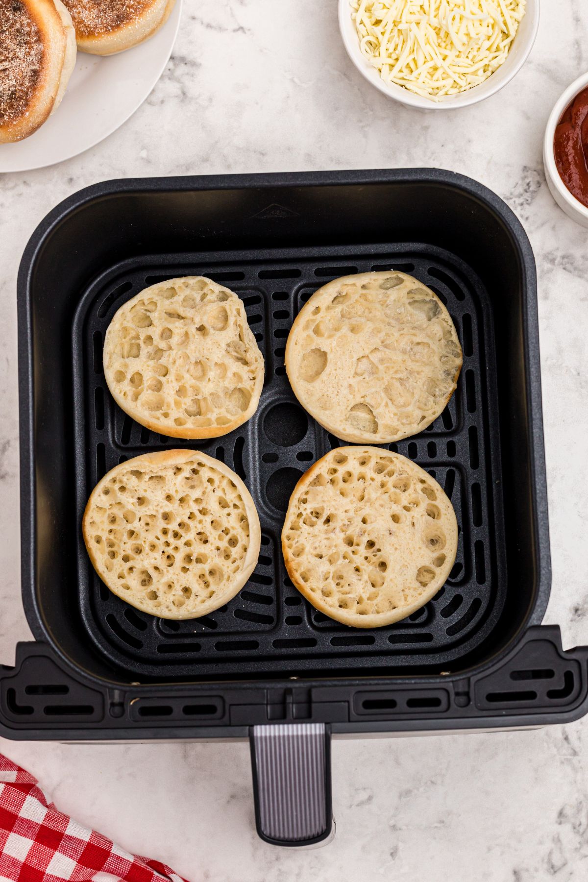 English muffins in the air fryer basket, being lightly toasted.