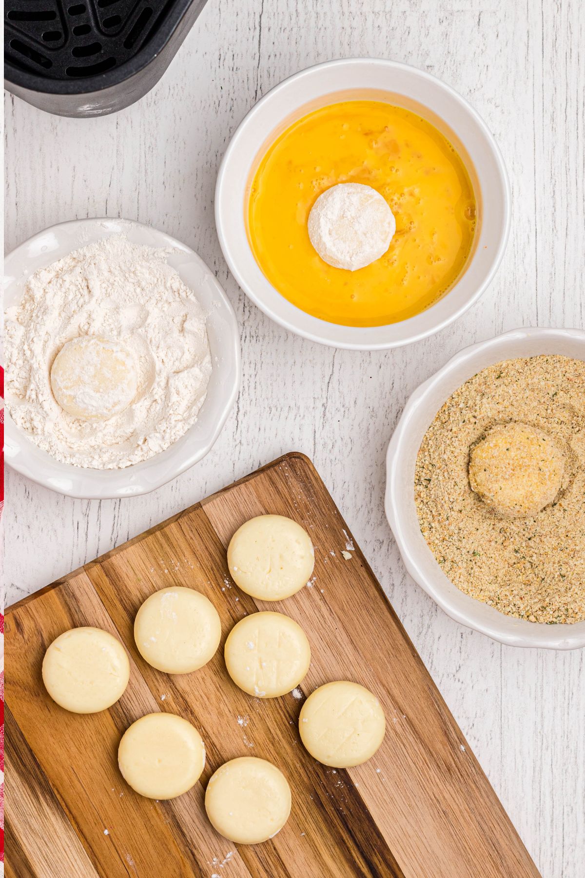Babybel cheese rounds being coated in flour, then dipped in whisked eggs, and coated in breadcrumbs.