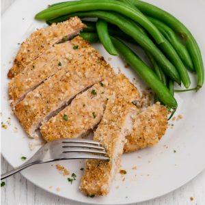 Overhead sliced air fried chicken breast with side of green beans on a white plate.