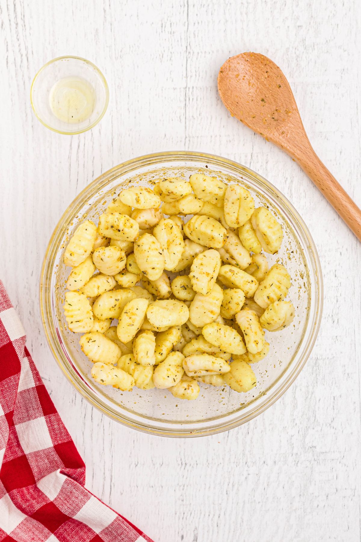 Golden gnocci tossed in olive oil and seasonings in a clear glass bowl.