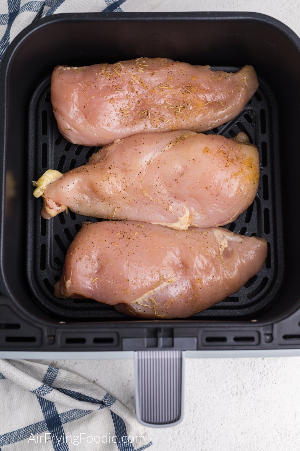 Seasoned chicken breast in a single layer on the air fryer basket.