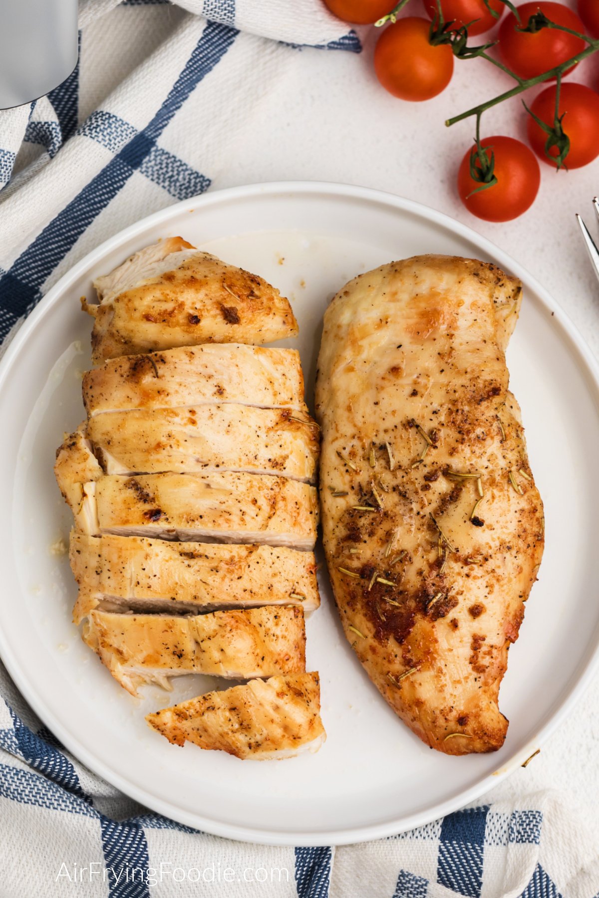 Seasoned, sliced, and whole grilled chicken breast made in the air fryer and served on a white plate.