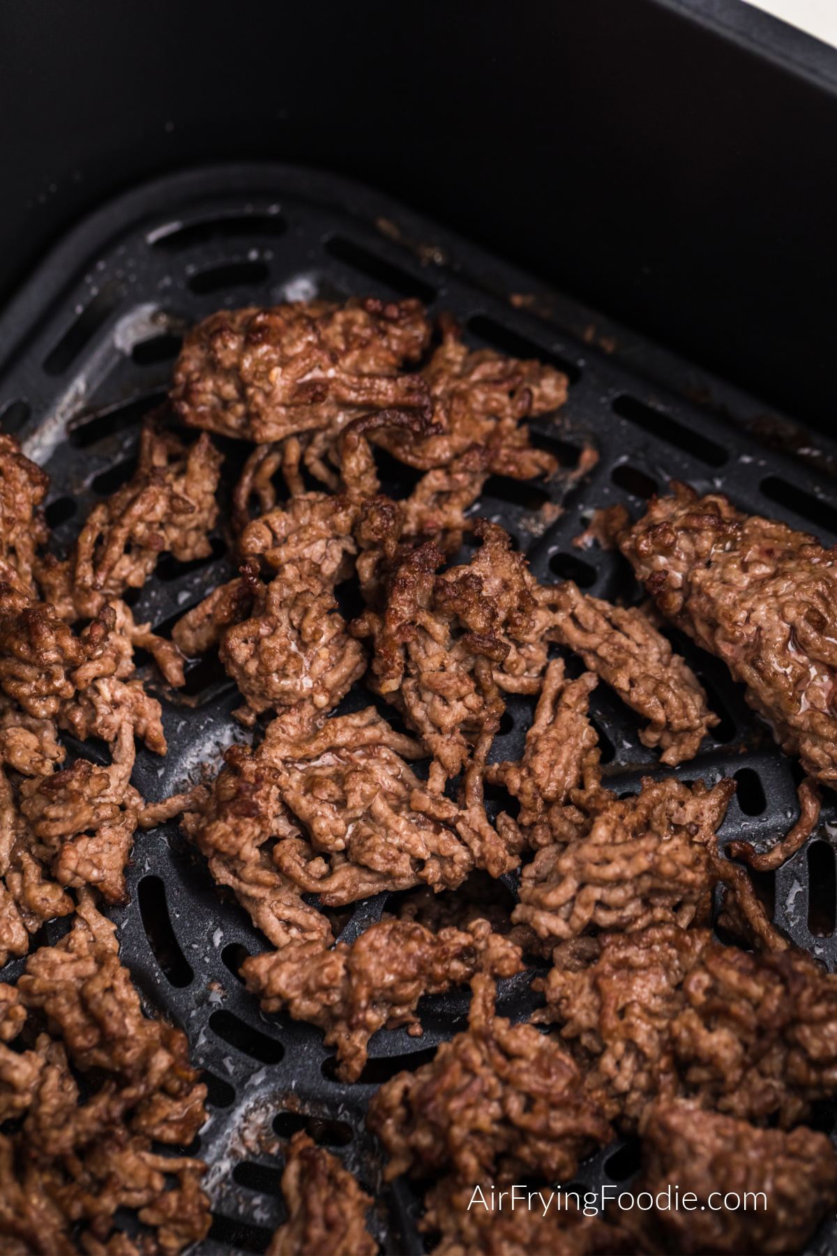 Close up photo of ground beef in the basket of the air fryer.
