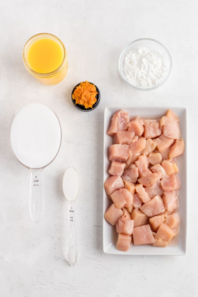 Ingredients needed to make orange chicken on a white marble table. 