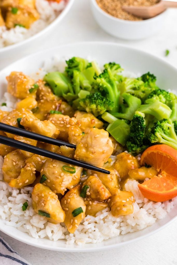 Golden orange chicken served over rice and with broccoli on a white plate. 