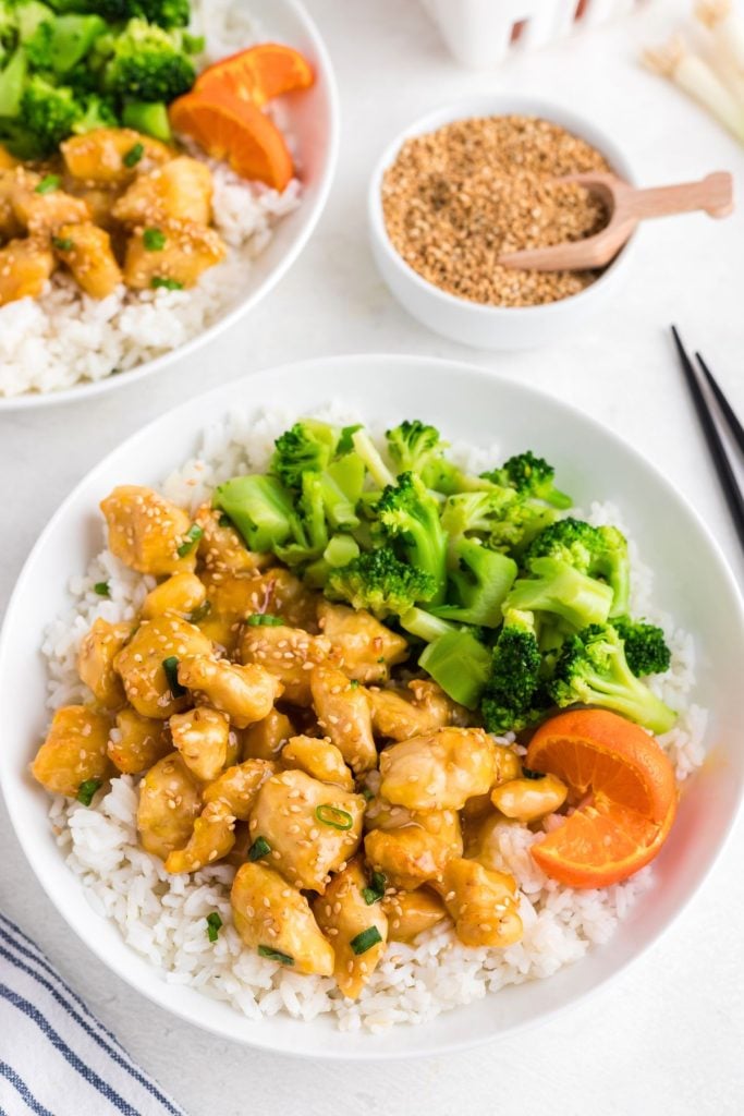 golden orange pieces of chicken covered in orange sauce on a white plate served with rice and broccoli