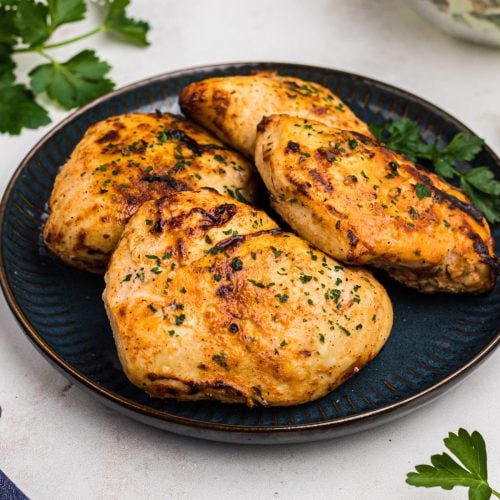 Golden juicy chicken breasts on a blue plate with parsley garnish.