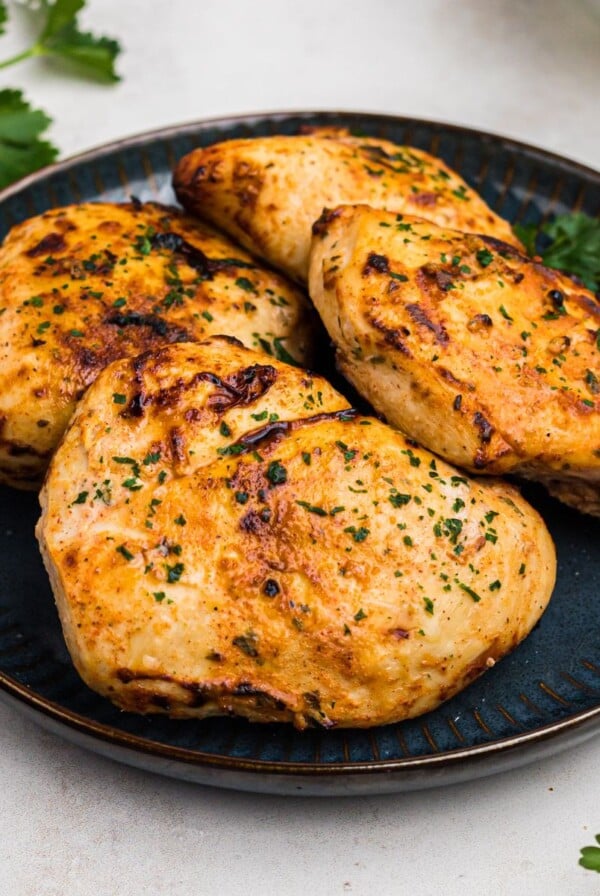 Golden juicy chicken breasts on a blue plate with parsley garnish.