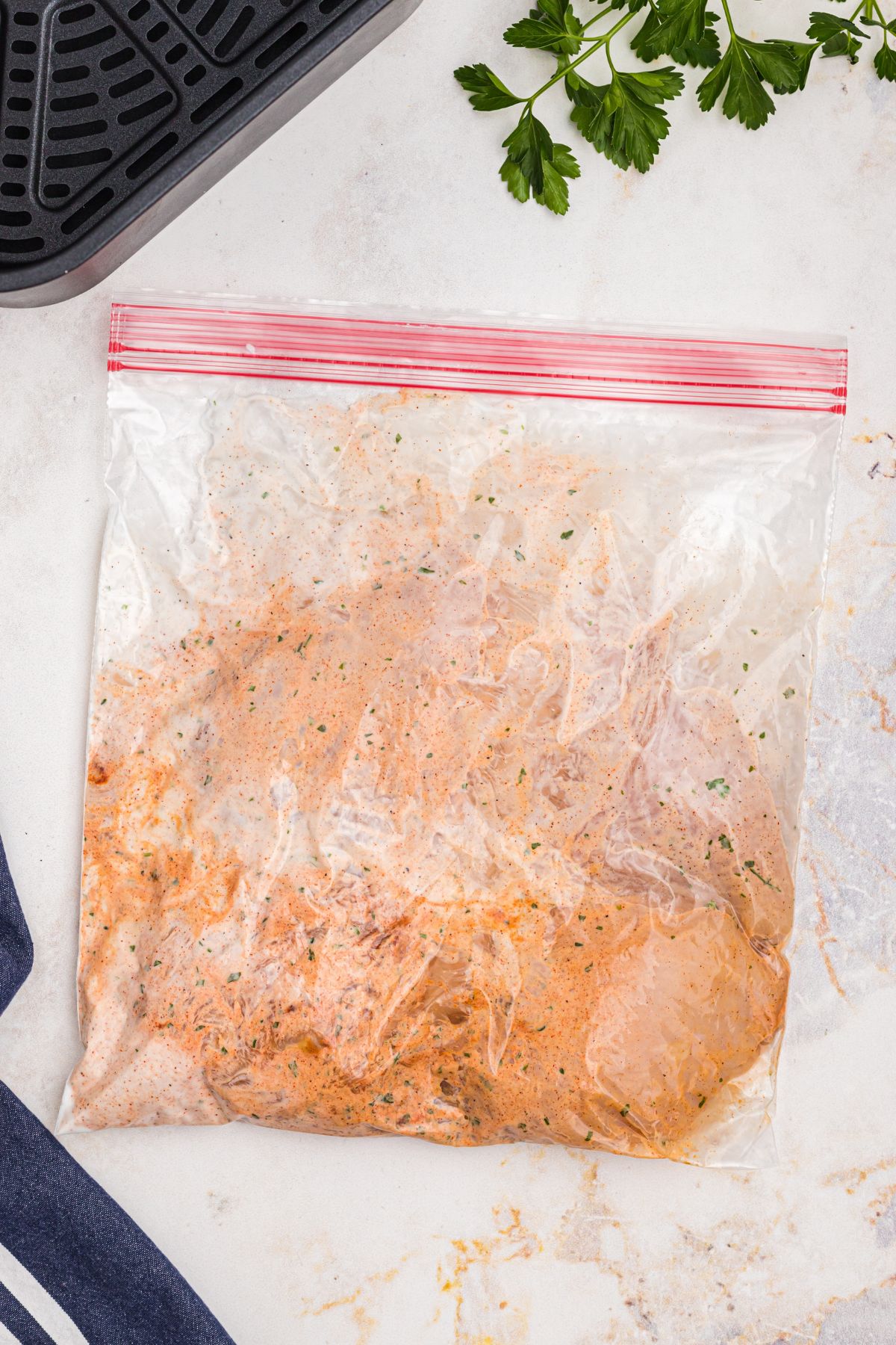 Ziploc bag filled with uncooked chicken breast, yogurt, and seasonings.