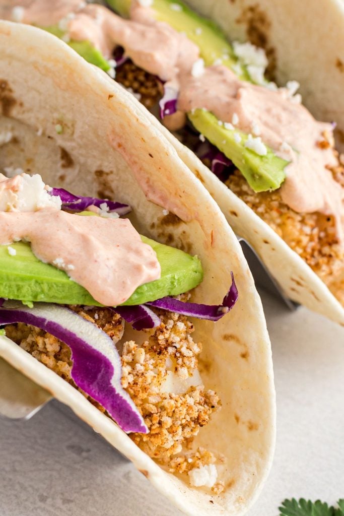Breaded fish in a flour tortilla topped with avocado, purple cabbage, and spicy sauce,