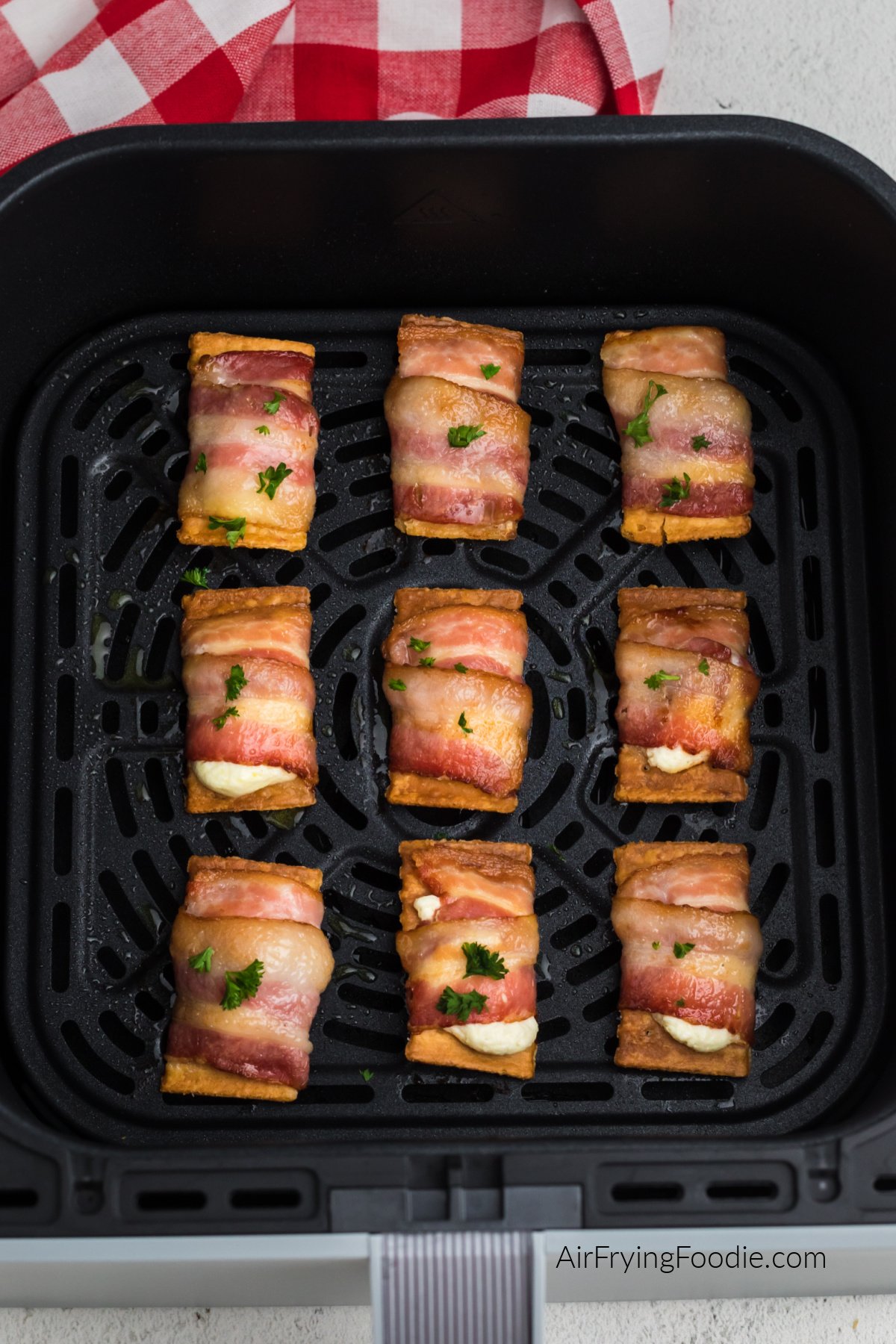 Air fried bacon wrapped cream cheese club crackers topped with fresh parsley in the basket of the air fryer.
