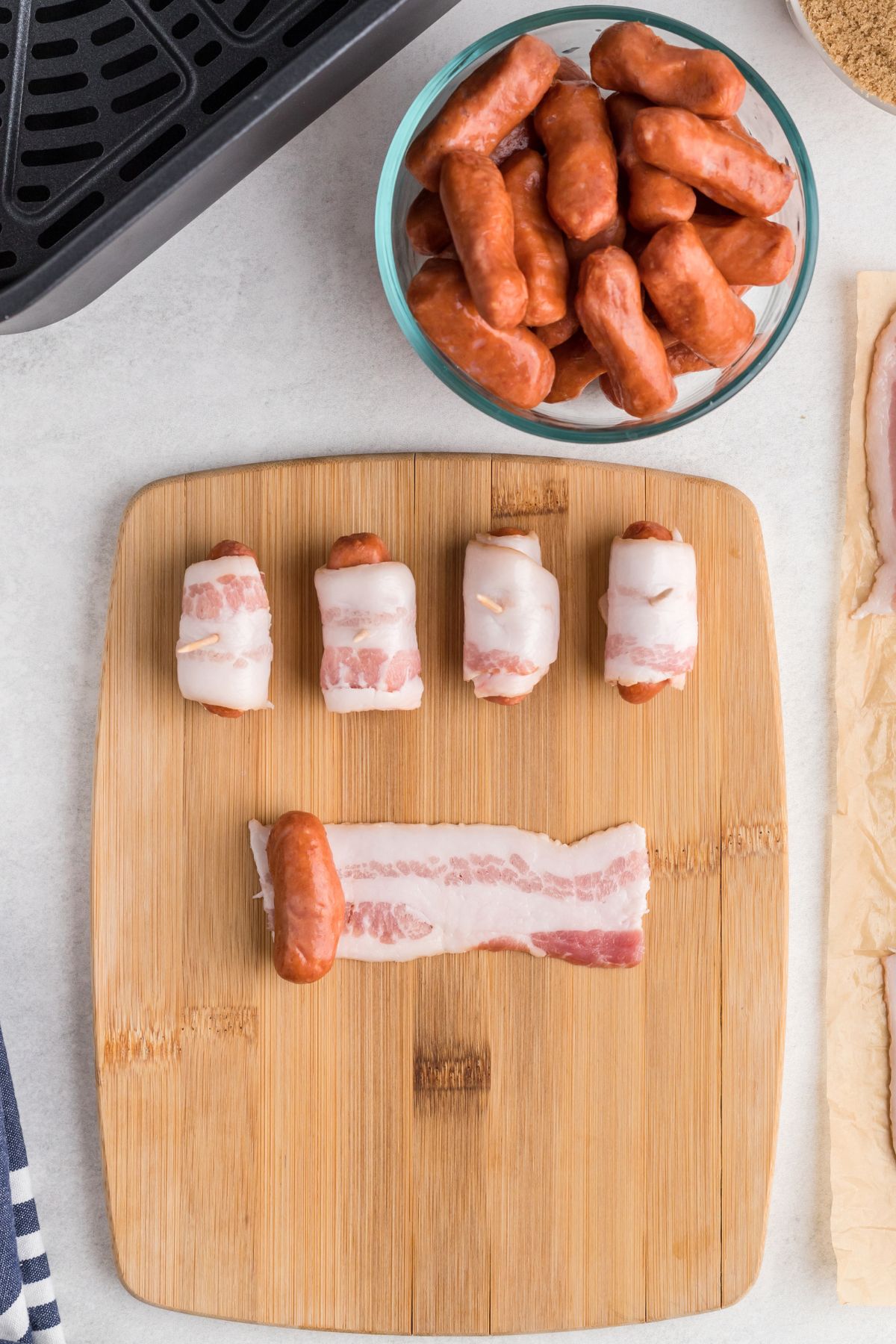 Bacon strips wrapped around smokies on a wooden cutting board
