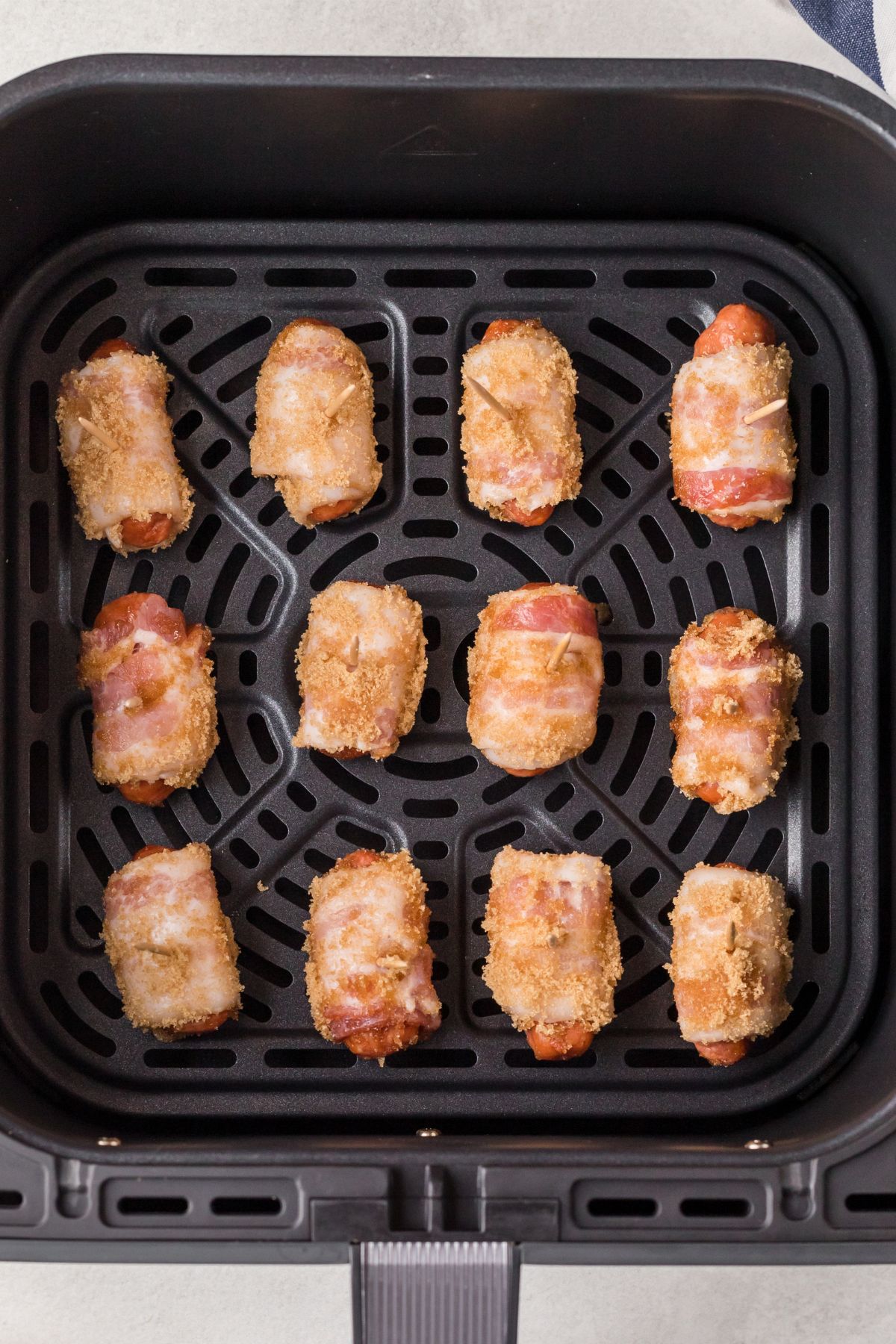 Bacon wrapped smokies, coated in brown sugar and placed in the air fryer basket.