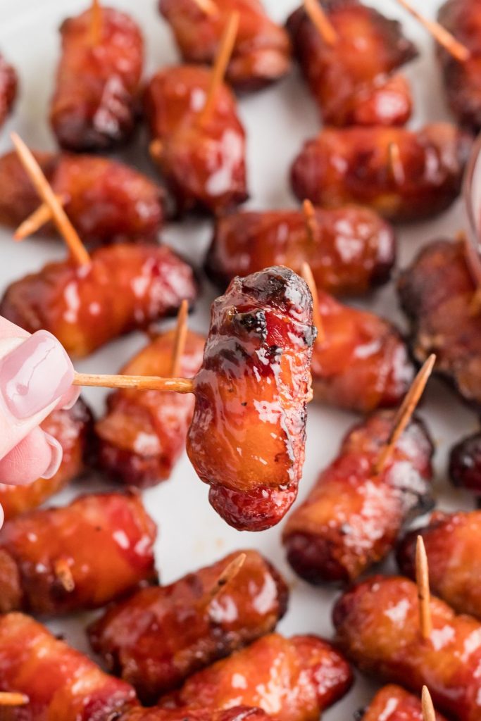 BBQ coated bacon wrapped smokies being held by the toothpick.