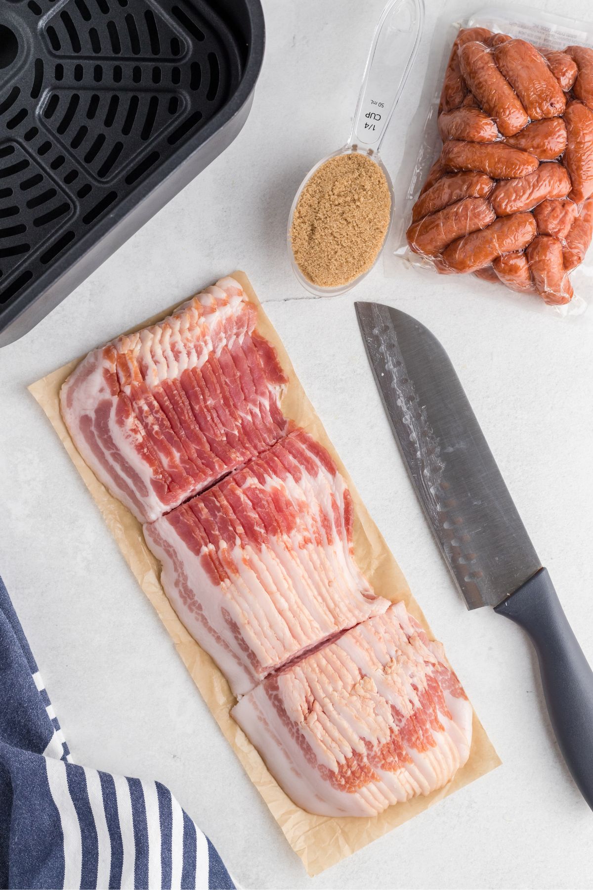 Uncooked bacon, cut into thirds in front of an empty air fryer basket.
