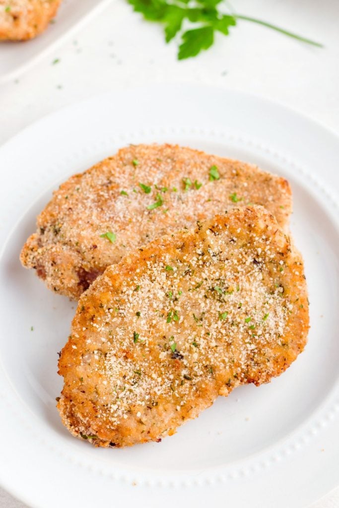 Golden brown breaded and seasoned pork chops on a white plate.