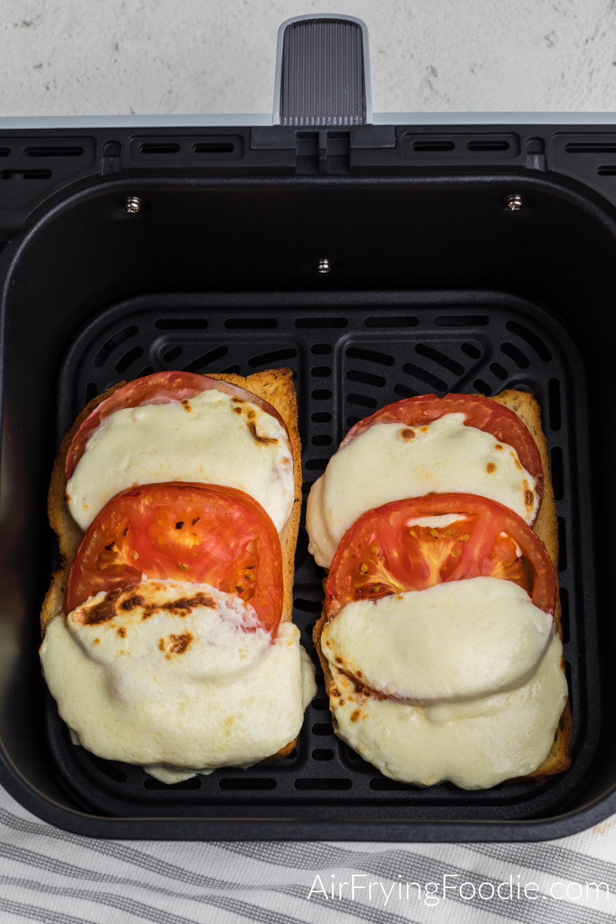 Tomato and grilled mozzarella cheese on buttered bread, air fried and in the basket of the air fryer.