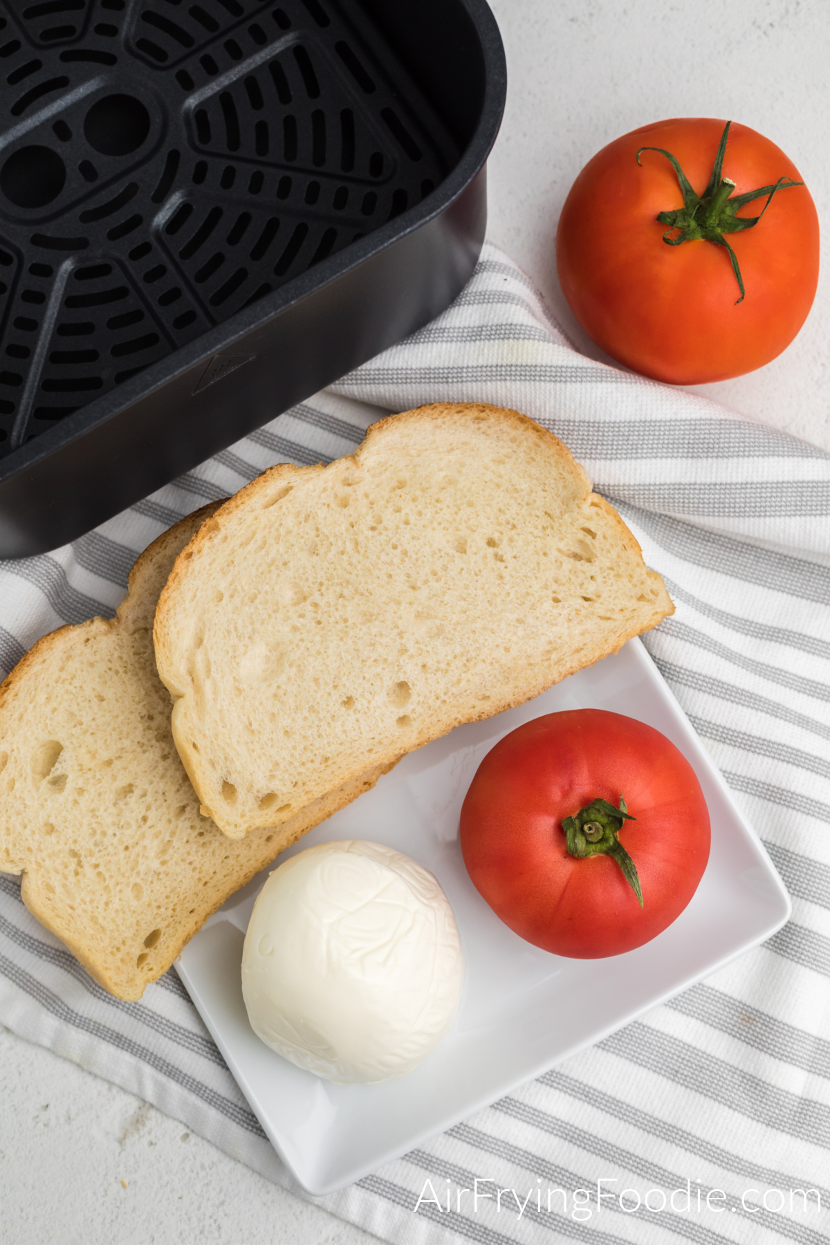 Mozzarella cheese, tomato, and bread on a white plate.