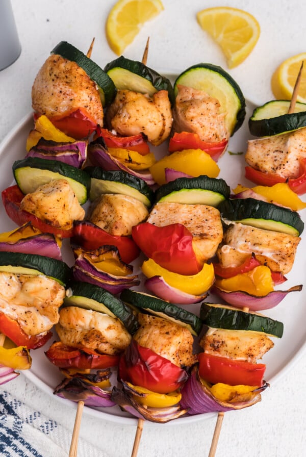 chicken kabobs made in the air fryer with lemon slices and served on a white plate.