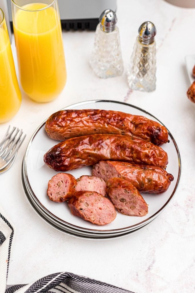 Chicken and apple sausage slices on white plates in front of an air fryer, and orange juice. 