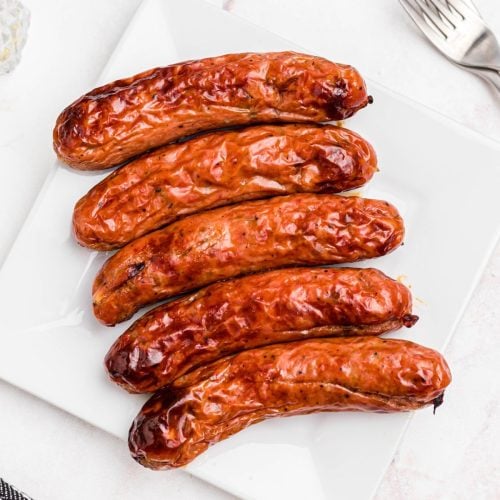 Juicy chicken sausages on a white plate after being cooked in the air fryer.