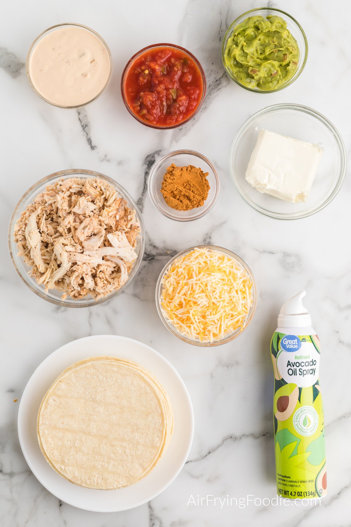 Ingredients and sauces needed to make homemade chicken taquitos laid out on a white table. 