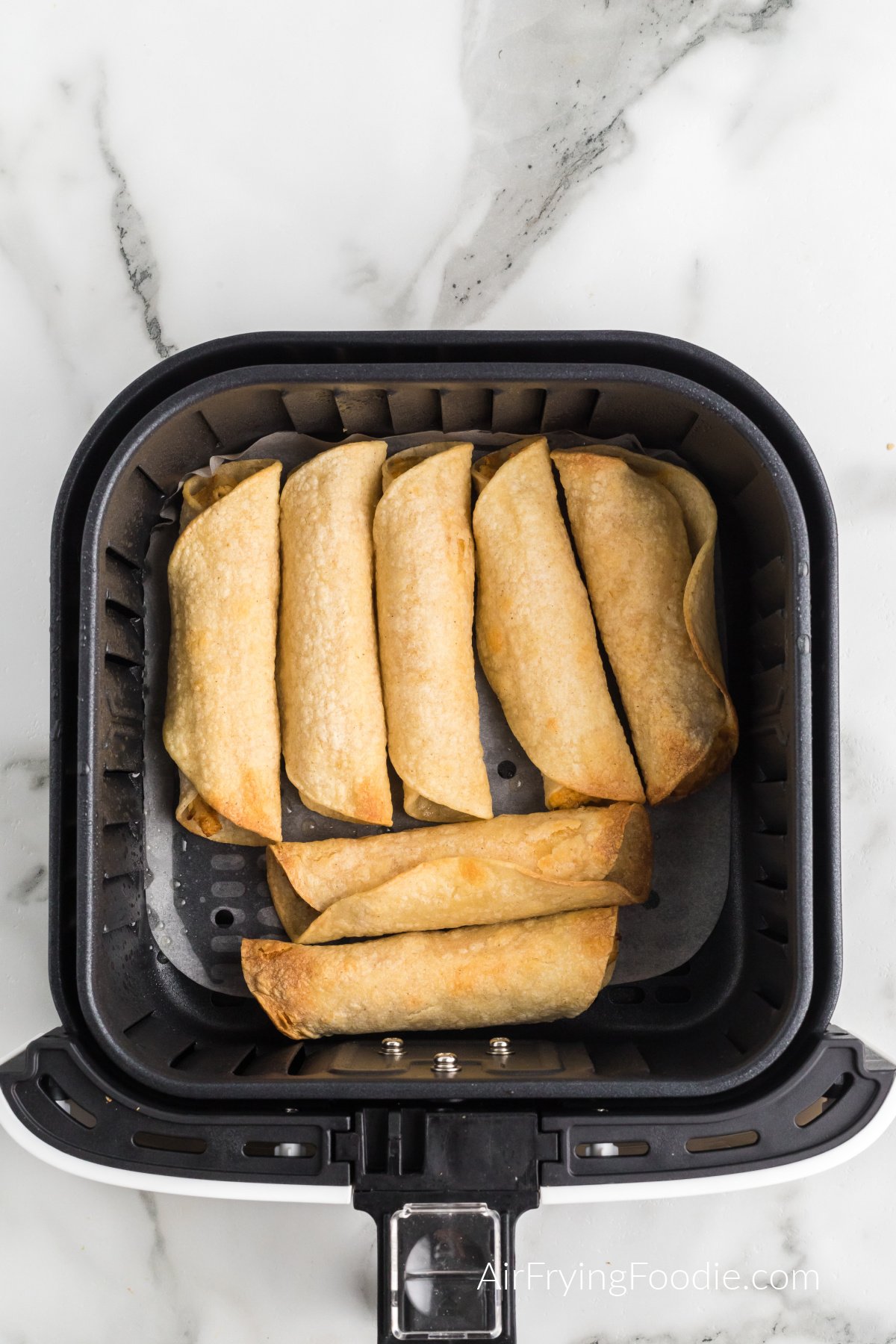 Air fried chicken taquitos in the basket of the air fryer.