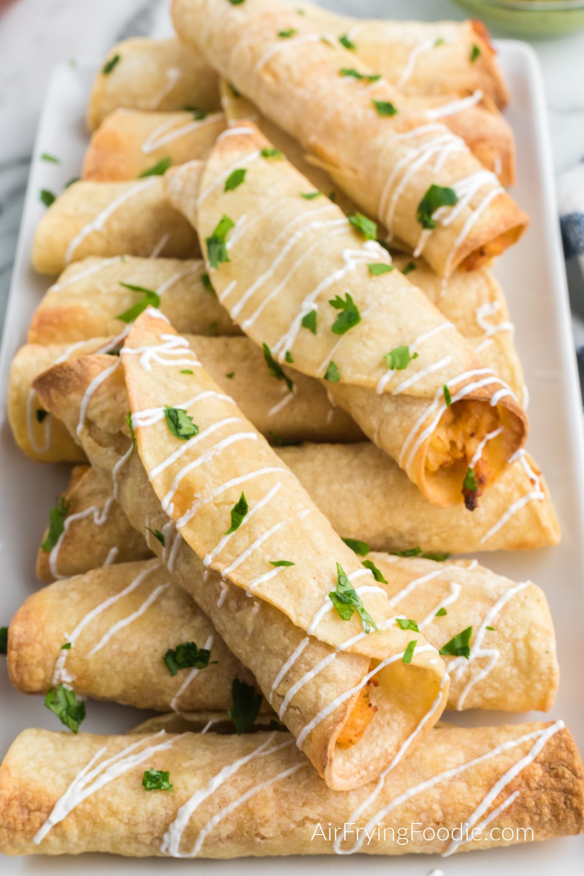 Chicken taquitos made in the air fryer, topped with sour cream and fresh cilantro.