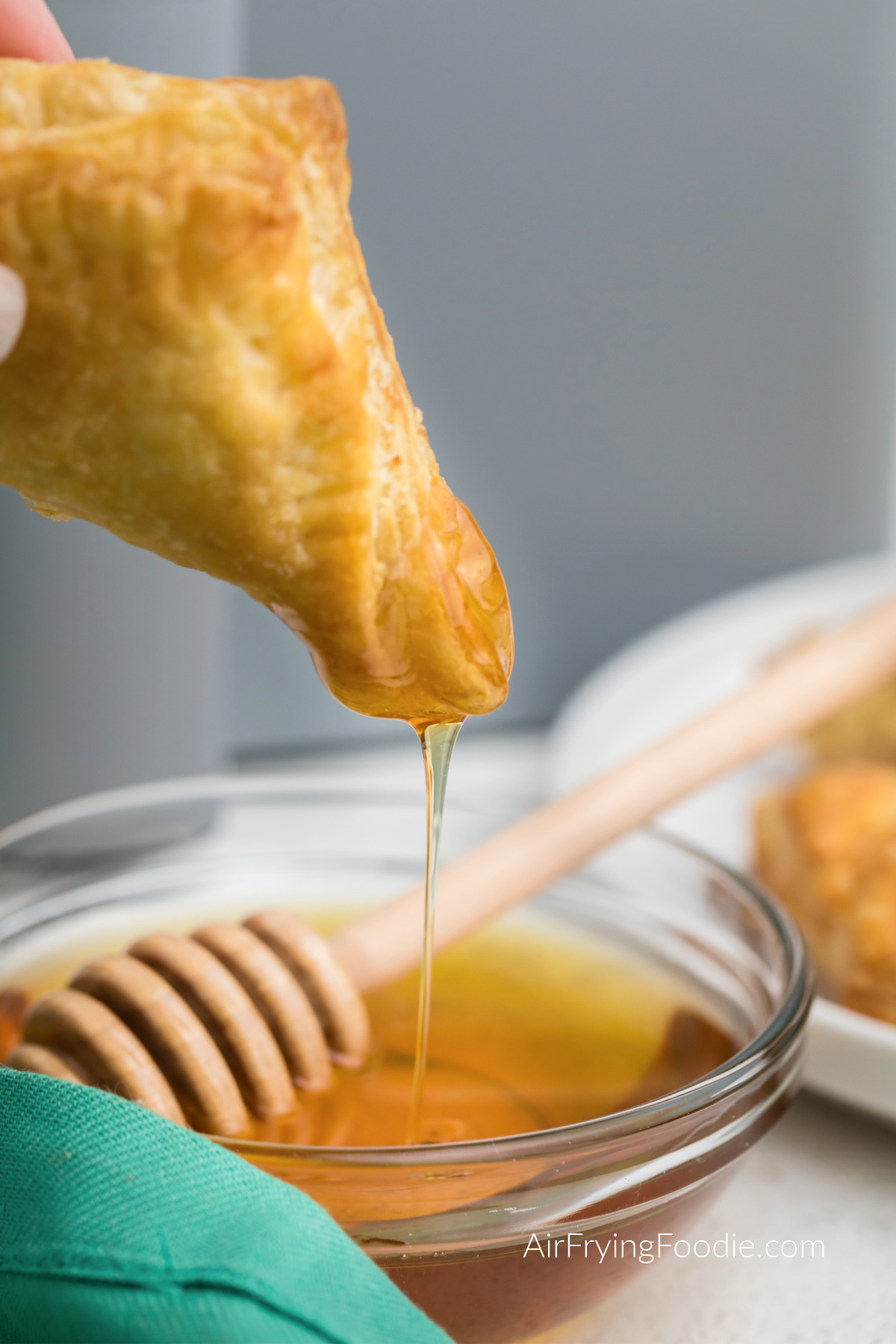 Cream cheese puff pastry being dipped into honey.