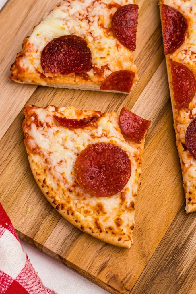 Golden crispy pepperoni pizza cut on a wooden cutting board. 