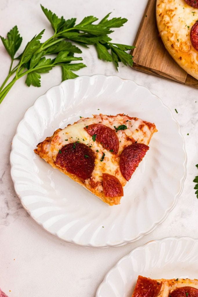 Golden crispy slice of pepperoni pizza on a small white plate. 