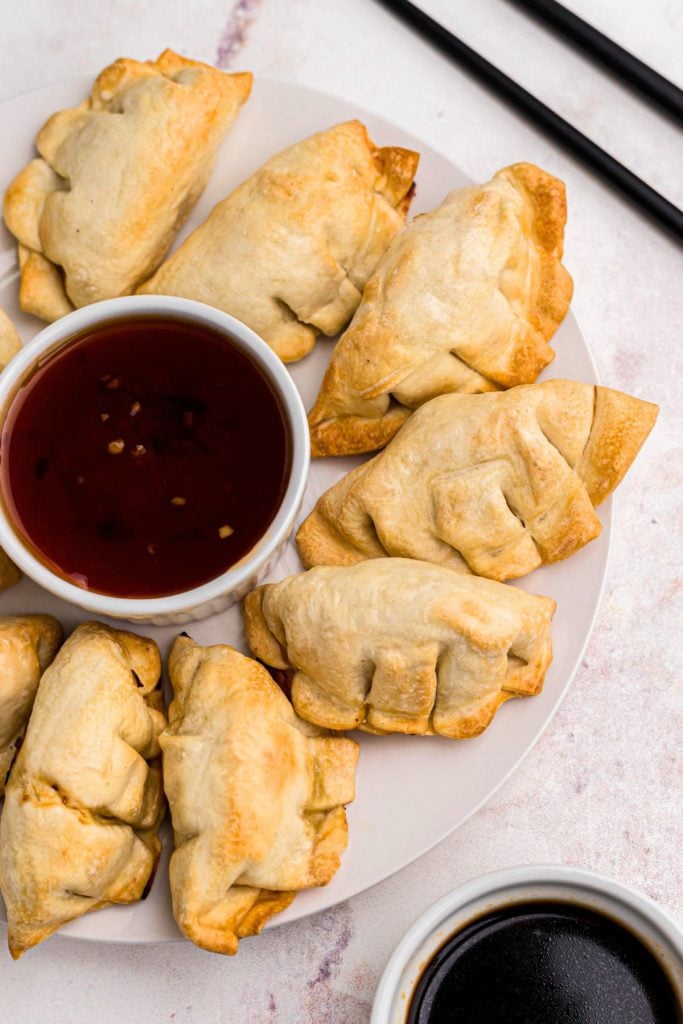 Golden crispy potstickers cooked on a white plate served with orange sauce and soy sauce. 