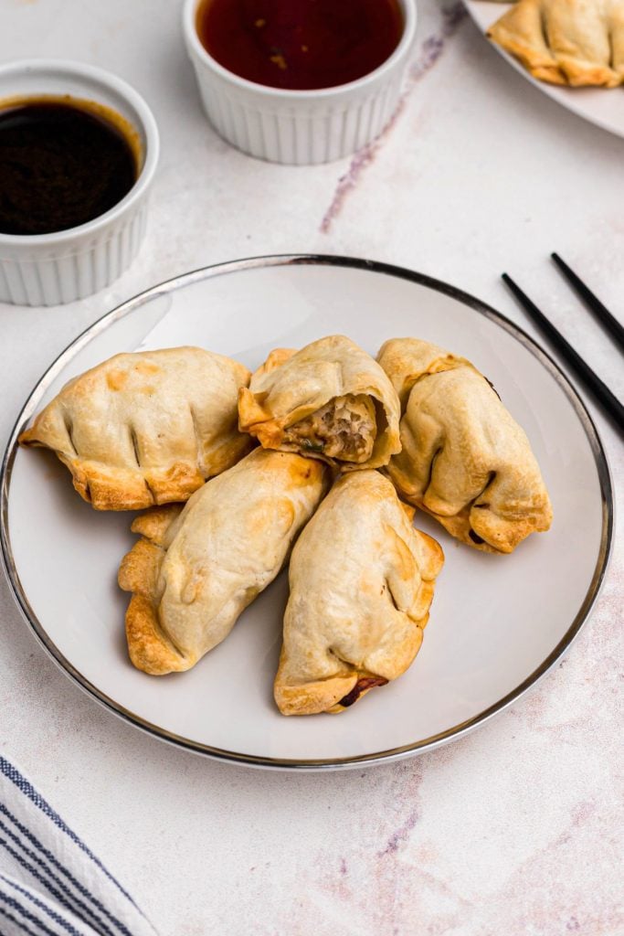 golden crispy chicken potstickers on a small white plate served with sauces. 