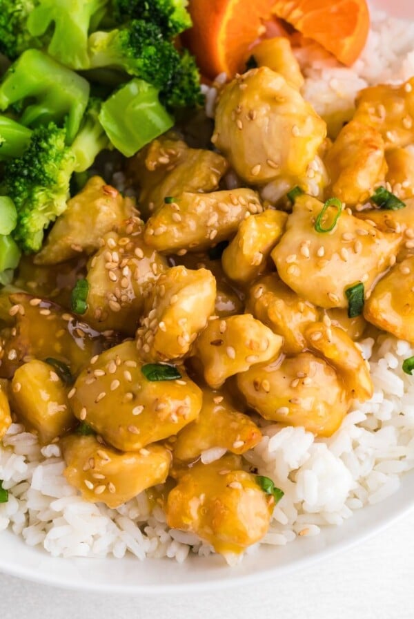 Juicy orange chicken served over rice with broccoli on a white plate.