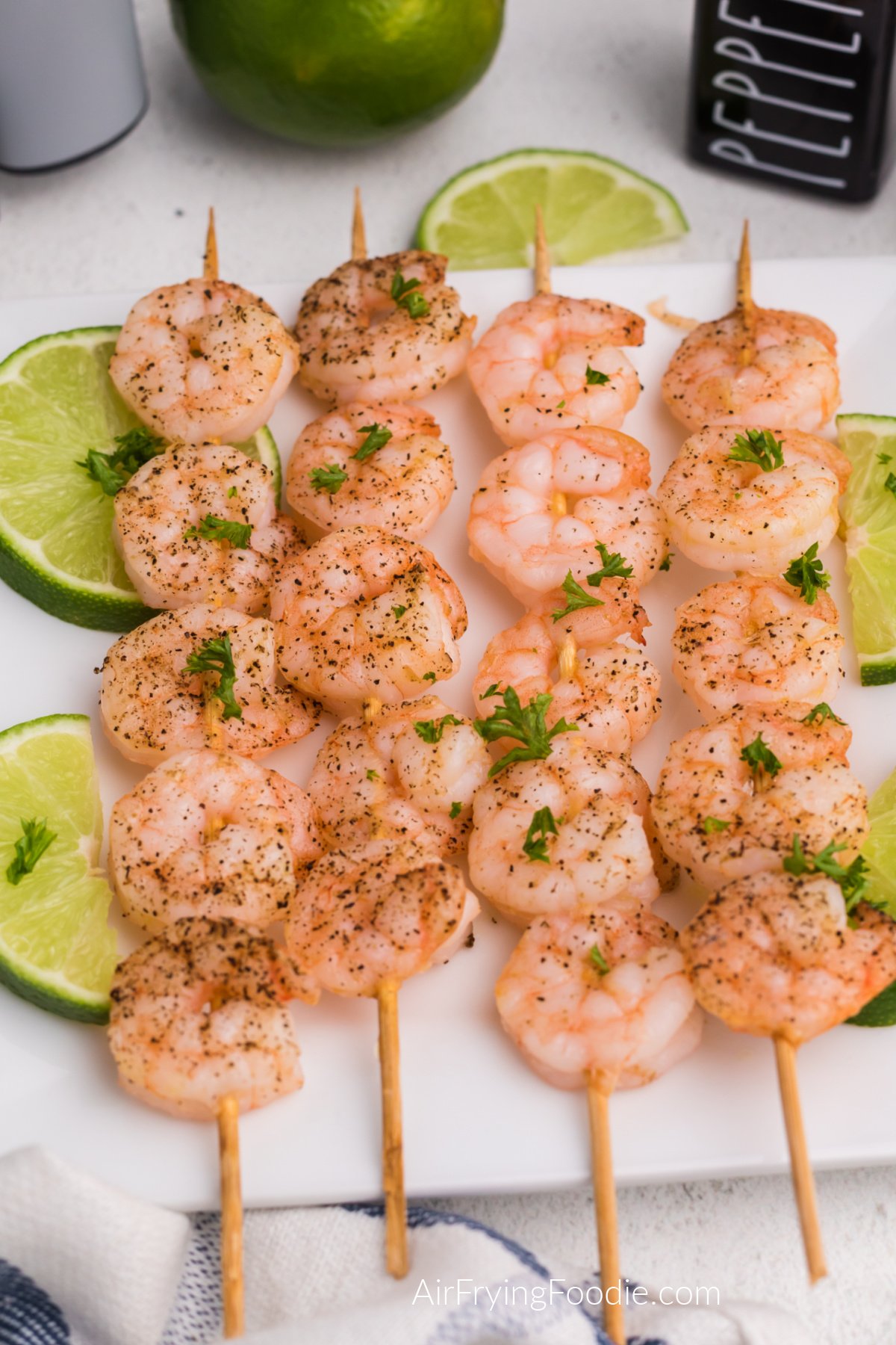 Air fried shrimp skewers on a white plate with sliced of lime.