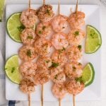 Overhead of shrimp skewers on a white plate with sliced limes.