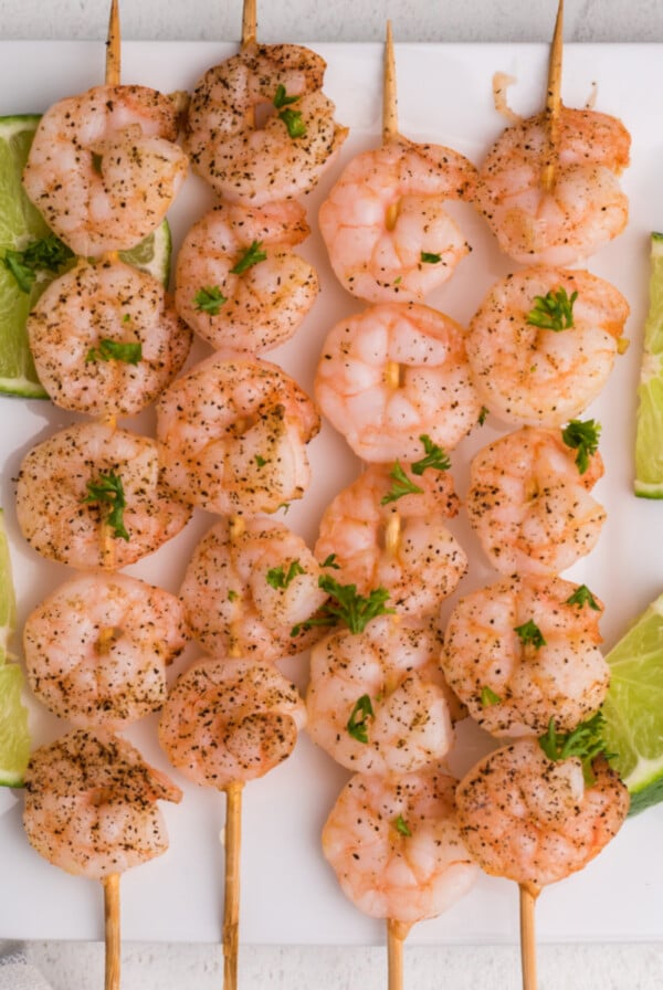 Overhead of shrimp skewers on a white plate with sliced limes.