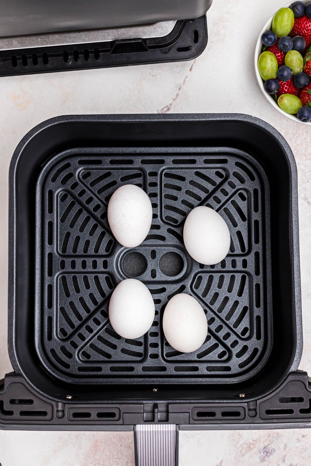 Four white eggs in shell, in the air fryer basket.