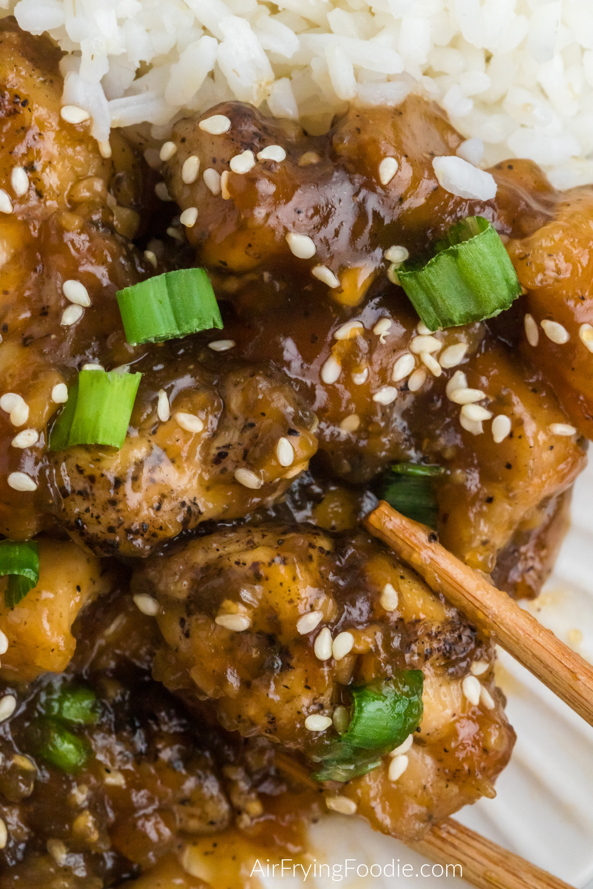 Close up photo of air fryer Teriyaki chicken topped with sesame seeds and green onions and served with chopsticks for eating.