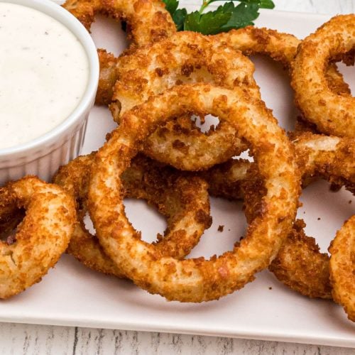 Golden crispy onion rings on a white plate served with ranch dressing.
